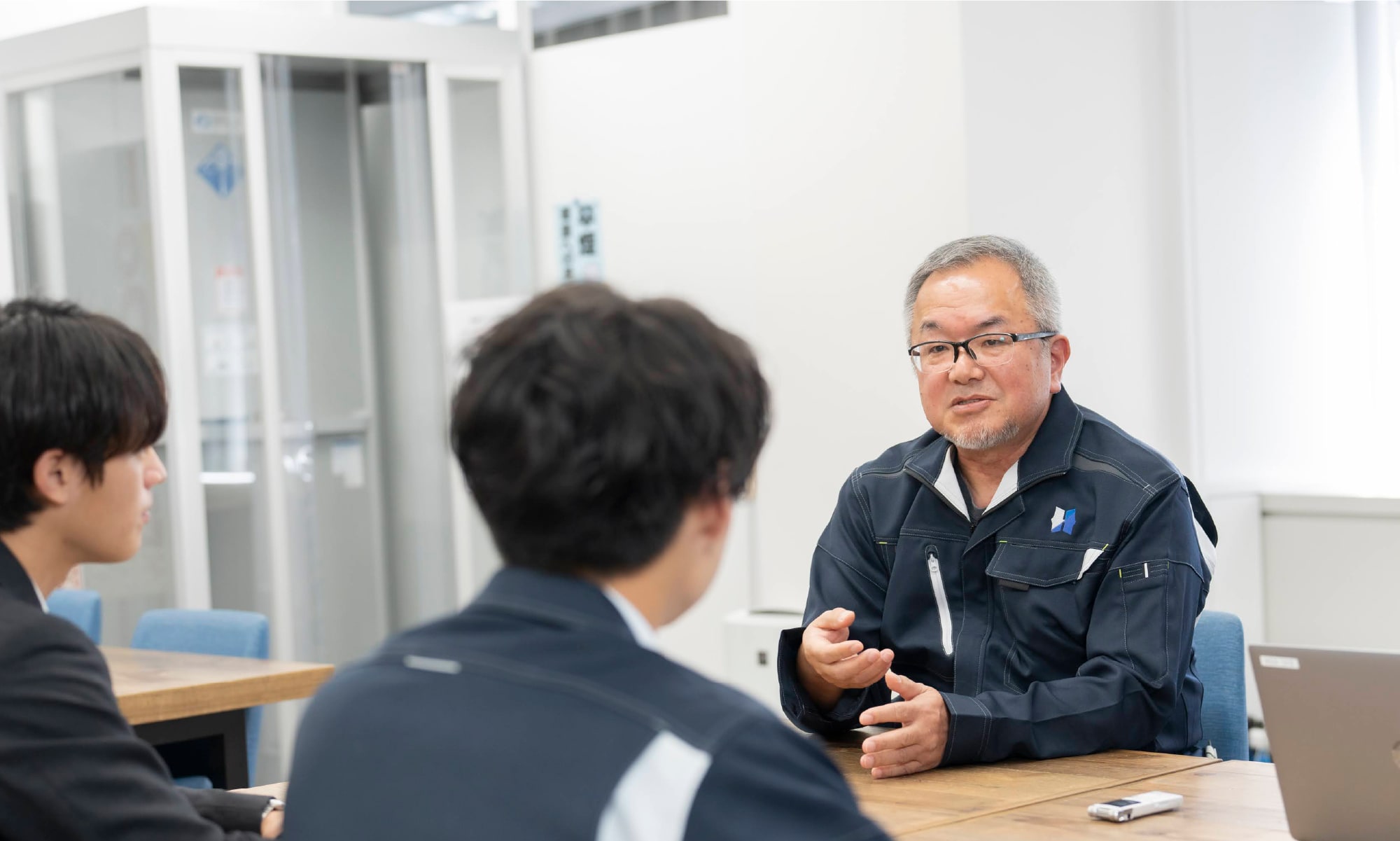 ジェスチャーを交えながら話す先輩社員と真剣に話を聞く若手社員